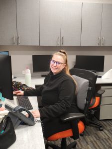 Eliza smiling while seated at a desk in a professional office environment