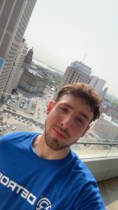 Demetrios standing on a balcony with a city skyline in the background.