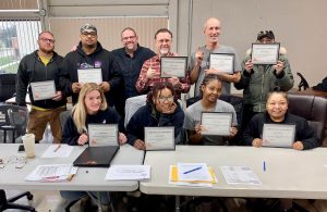 Group of Drake Enterprises employees holding training completion certificates.
