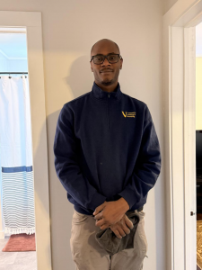 Shamar standing indoors in his work uniform, smiling at the camera.