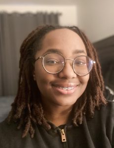 Breanna smiling in a close-up photo, wearing glasses and a black jacket