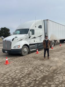 Blake standing in a training lot with a semi-truck and traffic cones during CDL training