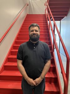 Cameron smiles at the camera while standing in front of a bright red staircase.