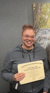 Mariah smiling at the camera holding her apprenticeship certificate